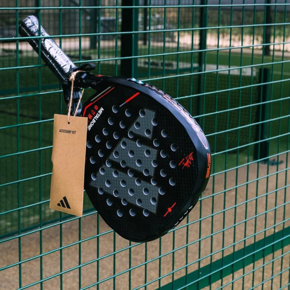 Axelblu Ltd Adidas Metalbone 2026 Ale Galan padel racket with carbon fibre texture hanging on a green court fence